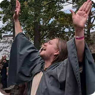 Ric Heise with his arms raised wearing a cloak. 