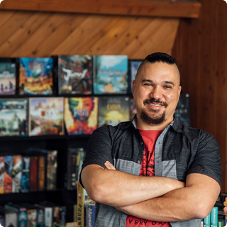 David Plamondon standing in front of a many boardgames on a shelf.